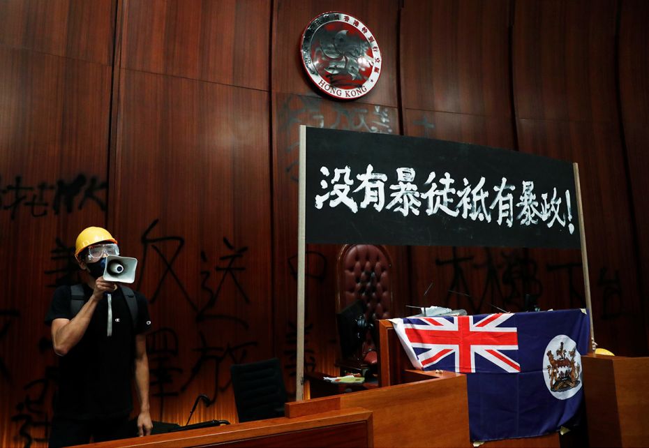 July 1, 2019: A man uses a loudspeaker as he stands next to a colonial flag of Hong Kong and a banne