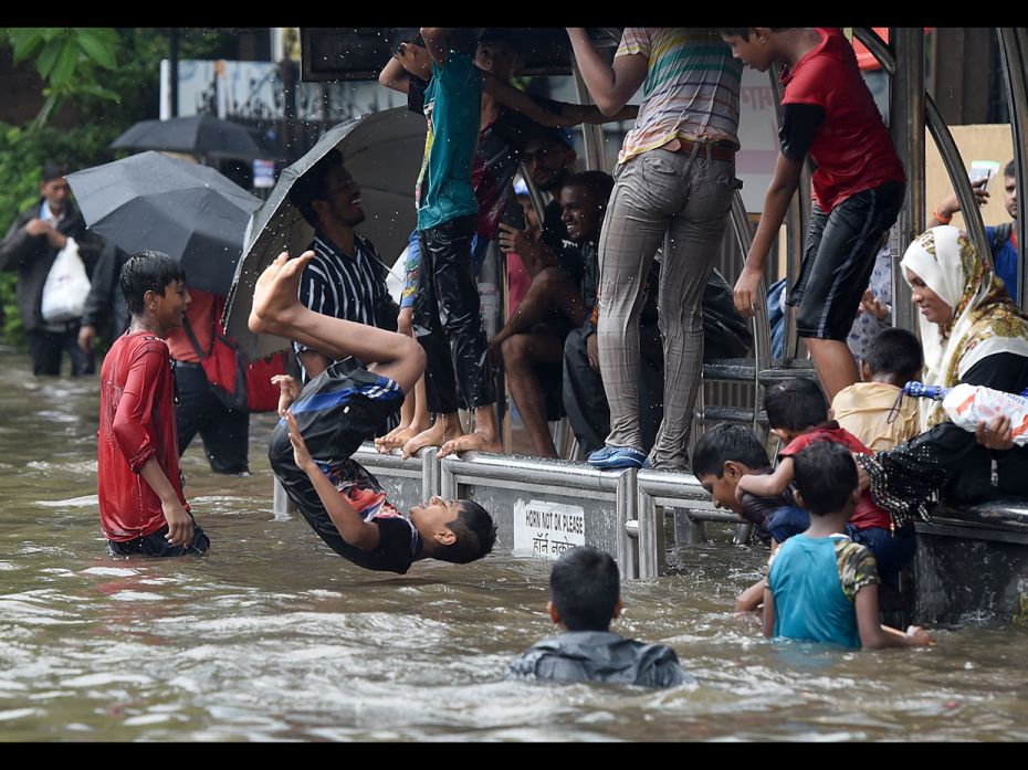 An Indian boy jumps into the water of a flooded street after heavy rain showers in Mumbai on July 1,