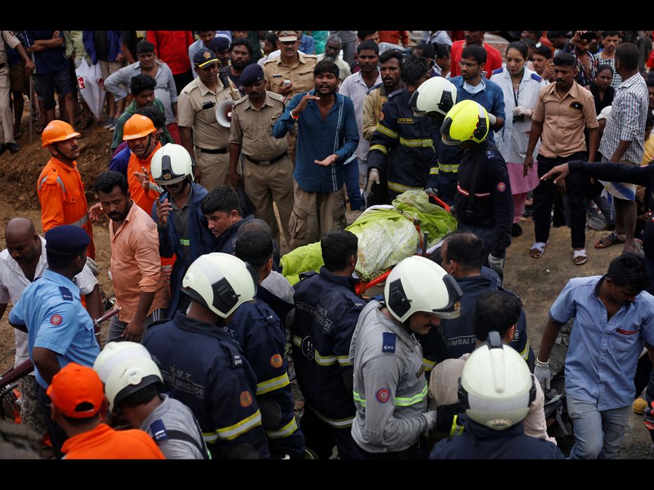 Rescue workers carry the body of a victim after a wall collapsed on shanties due to heavy rains at a