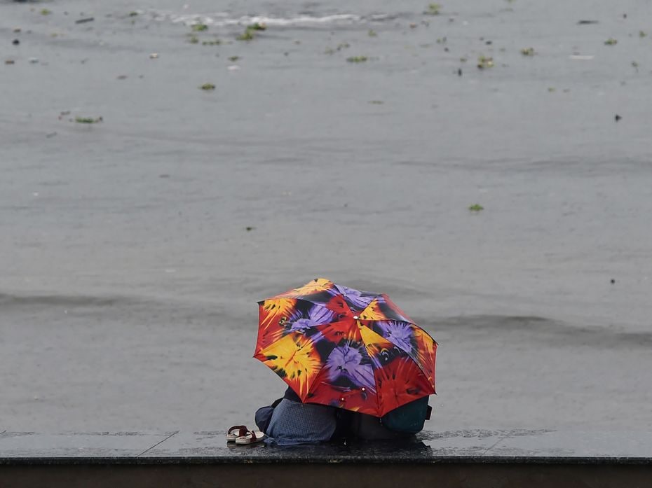 An Indian couple sit under an umbrella during monsoon rain showers at the seafront in Mumbai.