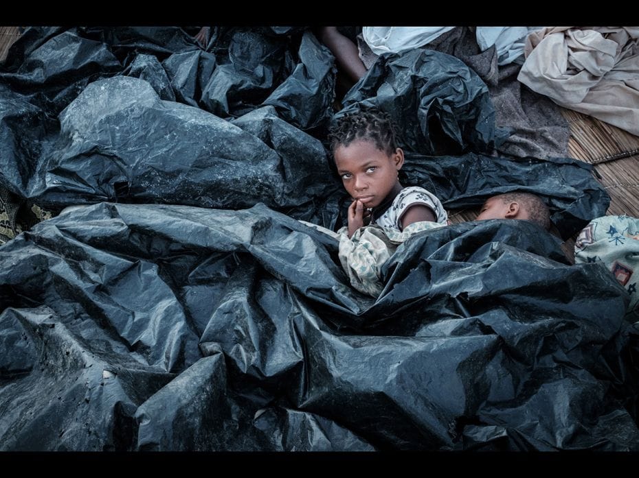 Enia Joaquin Luis, 11, wakes up beside her sister, Luisa, 6, under plastic sheets as they protect th