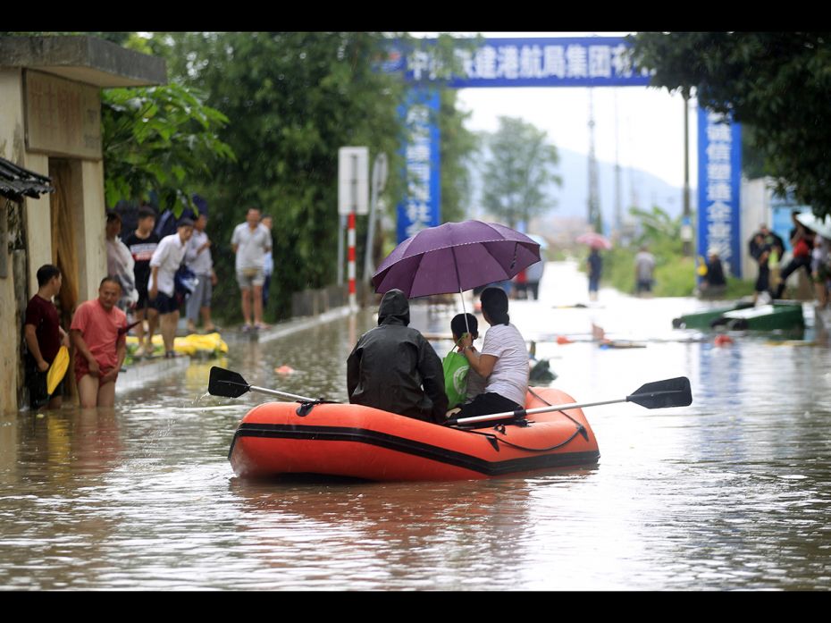 People row a rubber boat on a flooded road caused by a rainstorm at the Hongqi town on May 27, in Zh