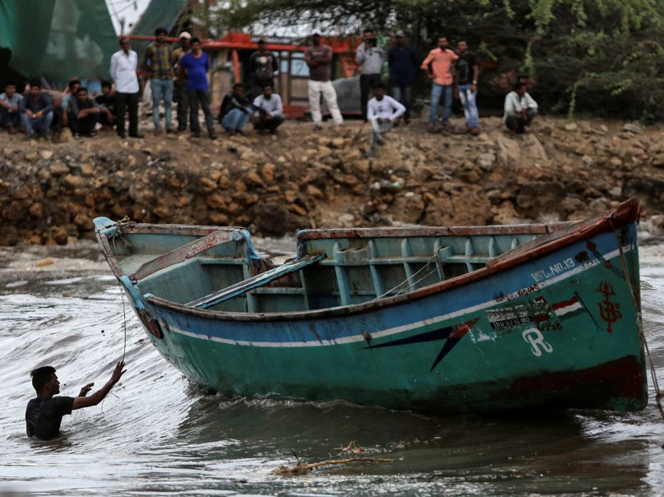 A fisherman wades through the water to rescue his fishing boat along the shore.