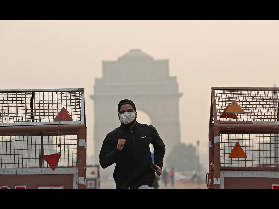 NEW DELHI, OCTOBER 28: A man wearing a mask runs past the India Gate on a smoggy morning in New Delh