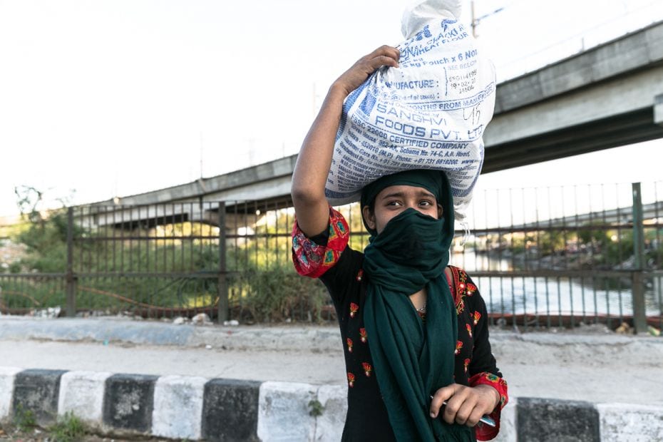 Muskaan walks on an empty road in Kalindi Kunj with provisions on her head, turning occasionally to 