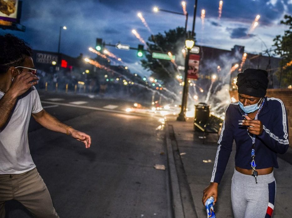 DENVER, CO - MAY 31: People react as tear gas canisters explode behind them while marching along Col