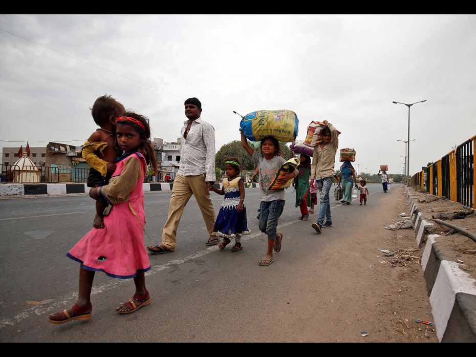 Migrant workers walk with their children as they look out for transport to return to their villages,