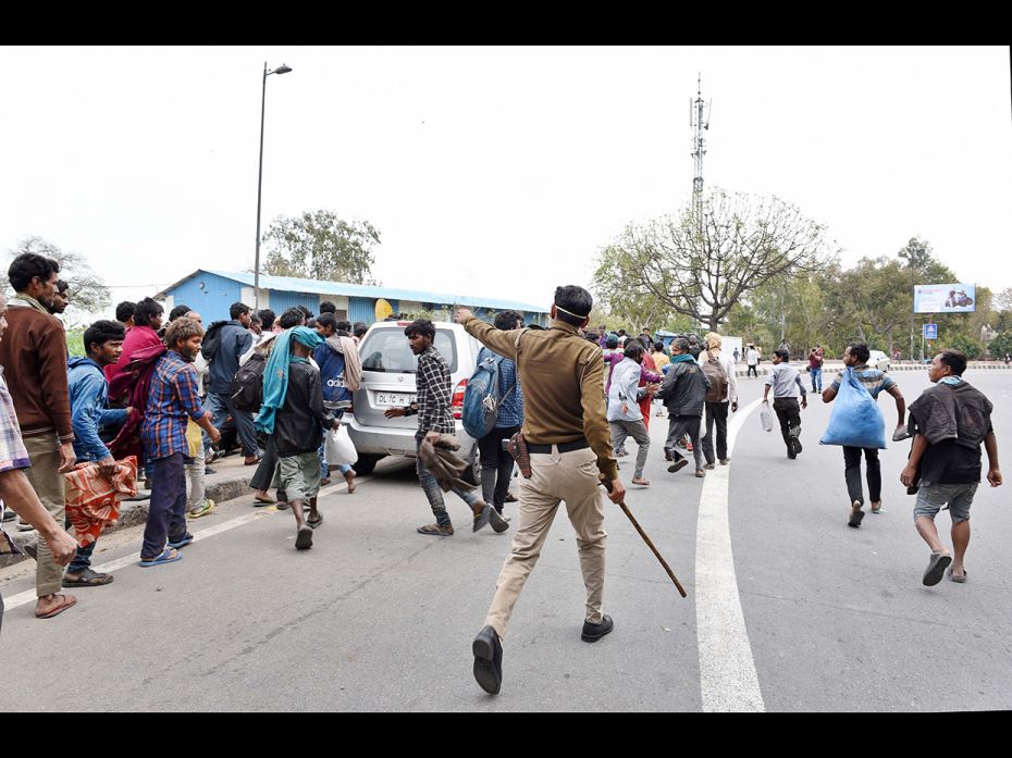 A Delhi police personnel disperse homeless people waiting to collect food at a government-run Night 