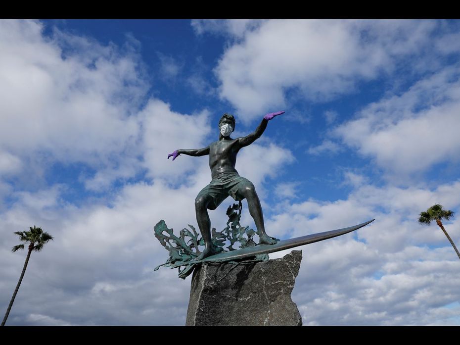 A surfer statue along the beach is decorated by pranksters with a mask and gloves during the global 