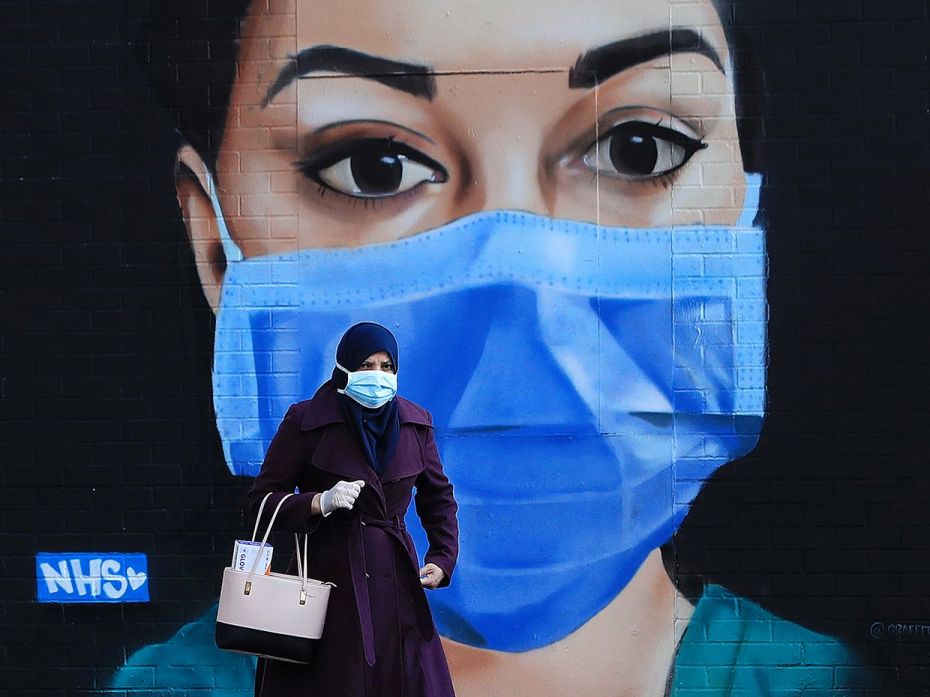 LONDON,      ENGLAND: A woman wearing a face mask walks past a piece of  street art      depicting a