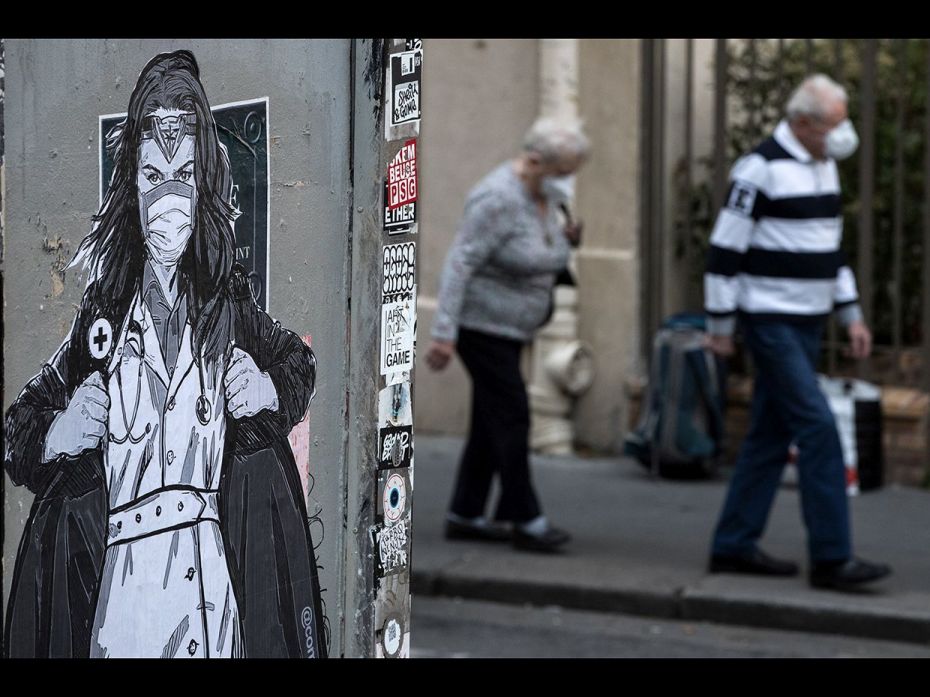 This      picture shows a masked elderly couple walking by a collage by  French      artist Combo in