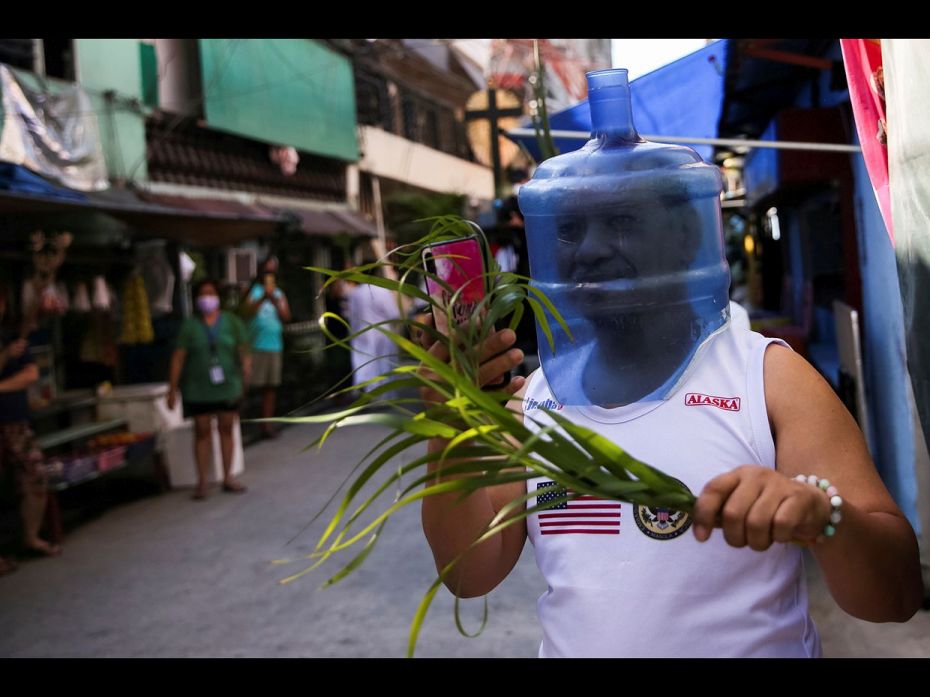 A man wearing makeshift protective head gear holds palm fronds outside his home as he waits for the 