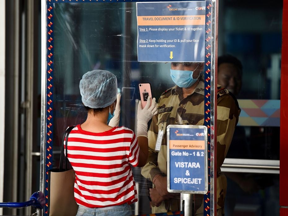 A security personnel checks a passenger’s documents while standing behind a shield at the Indi