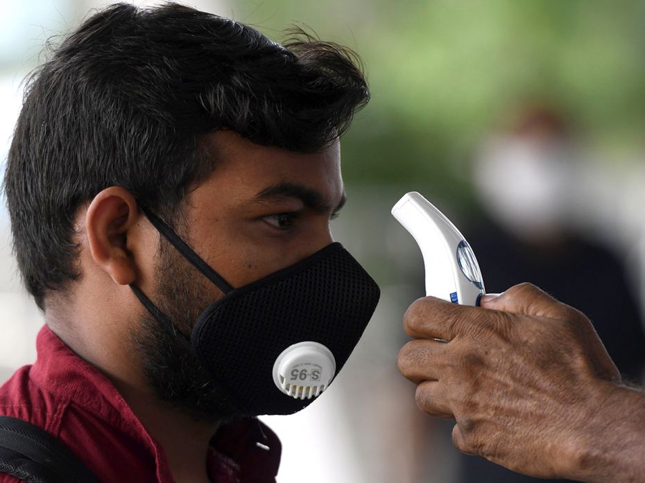 An airport staff member scans the temperature of a passenger at the Kamaraj domestic airport in Chen