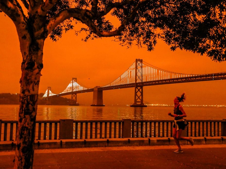 SAN FRANCISCO, CA - SEPT. 9: A woman jogs by the Bay Bridge as dark  orange skies hang over downtown