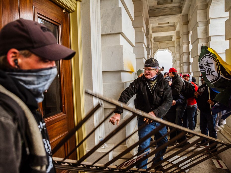 A member of a pro-Trump mob bashes an entrance of the Capitol building in an attempt to gain access 