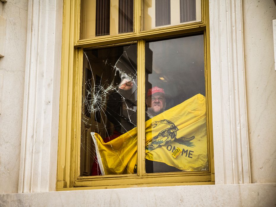 A member of a pro-Trump mob shatters a window with his fist from inside the Capitol Building after b