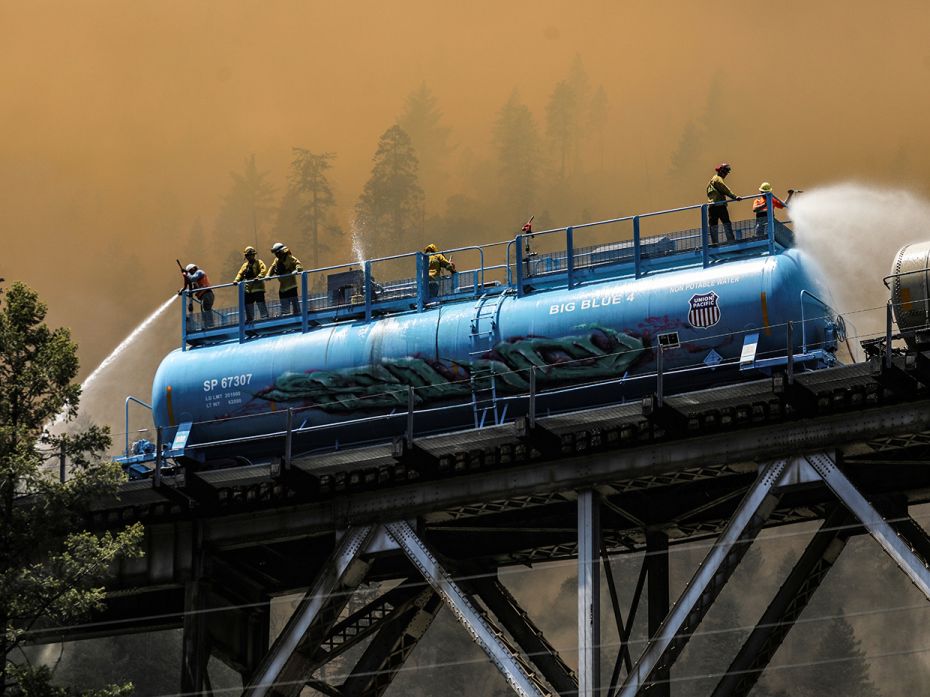 Firefighters spray water from a fire train to hot spots along the tracks over Rock Creek Bridge as t