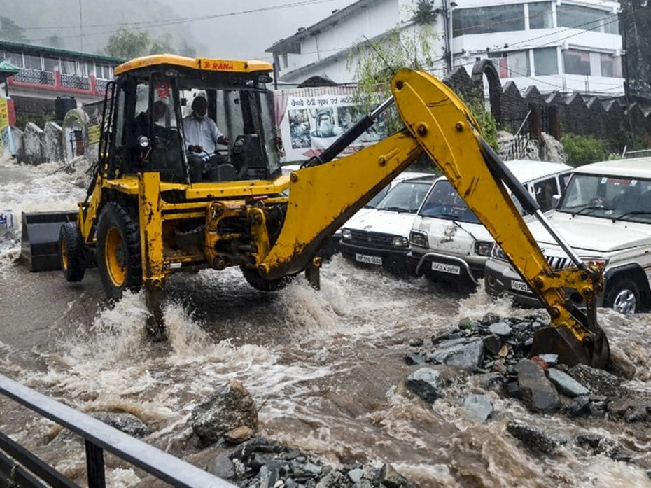 A worker uses an excavator to clear a road damaged by flash floods following heavy rains in Bhagsuna