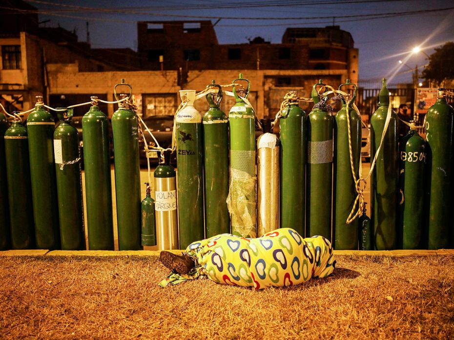 A person sleeps next to empty oxygen tanks to save a spot in the queue, as the supplier refills a ta