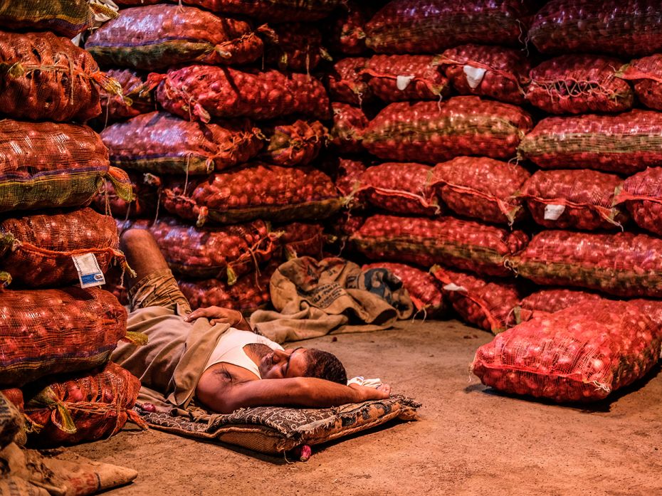 A vendor sleeping within sacks of onions in Koley market, one of the most crowded vegetable markets 