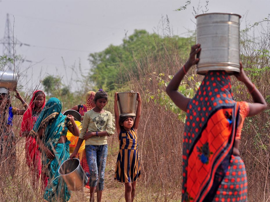 People carry water containers near an abandoned stone quarry on a hot day in Badama village in Allah