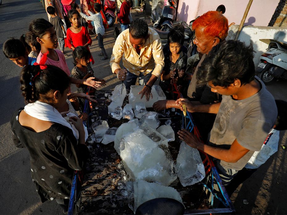 A man breaks a block of ice to distribute it among the residents of a slum during hot weather in Ahm