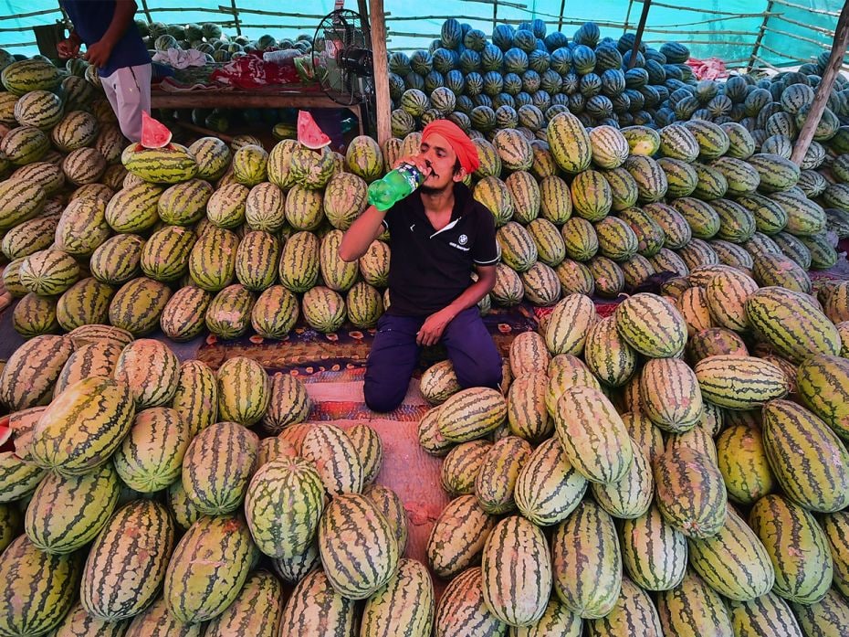 A watermelon seller drinks a cold drink as he waits for customers on a hot summer afternoon in Allah