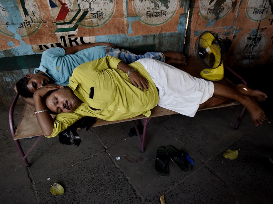 Two men sleep on a roadside bed with a table fan amid a heatwave in Kolkata, India, on April 25, 202