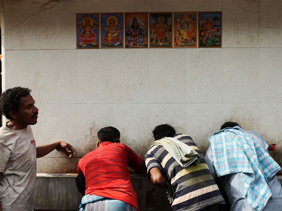 Labourers drink water from a public drinking water tap on a hot summer day in the old quarters of De