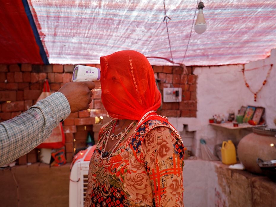 A healthcare worker checks the temperature of a woman inside her hut during a Covid-19 vaccinat