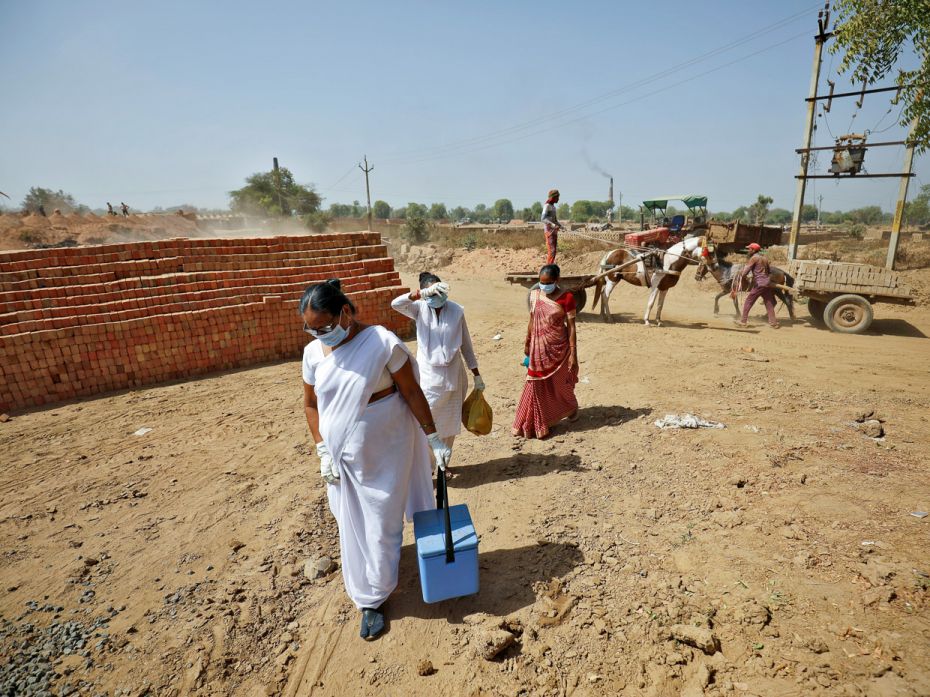 Healthcare workers walk among a brick kiln to administer the Covid-19 vaccine to kiln workers at Kav