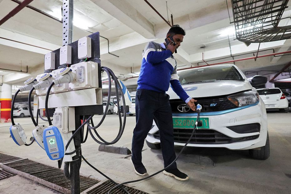 A man charges an electric vehicle at the charging hub of Indian ride-hailing BluSmart Electric Mobil