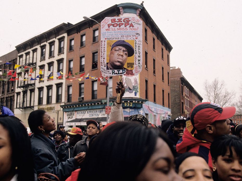 Police, neighbours, and fans follow the funeral caravan for rap artist Notorious BIG as it passes th