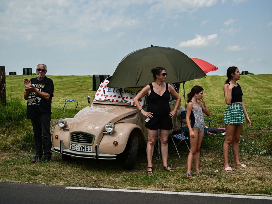 A family line the race route alongside a Citroen 2CV classic car during the 10th stage from Vulcania