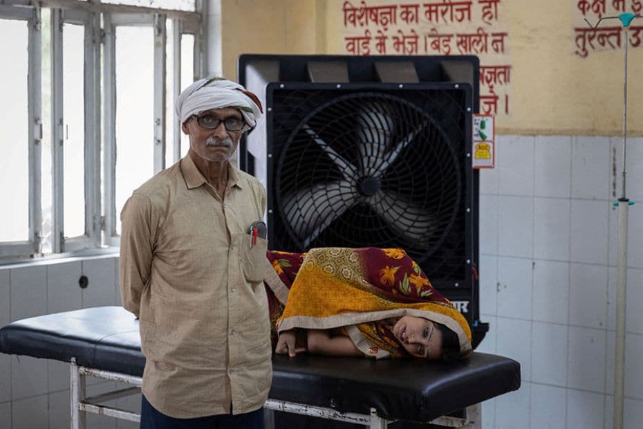 Suffering from heat-related illness, Reshmi Pathak lies on a stretcher as her father stands next to 