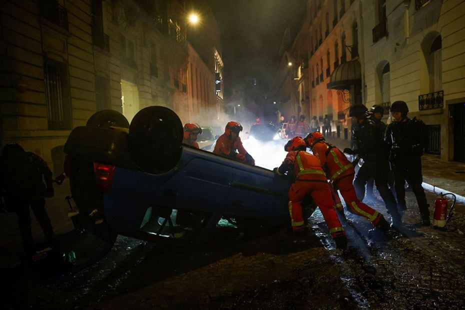 French riot police officers and emergency personnel work to move a vehicle during the fifth day of p