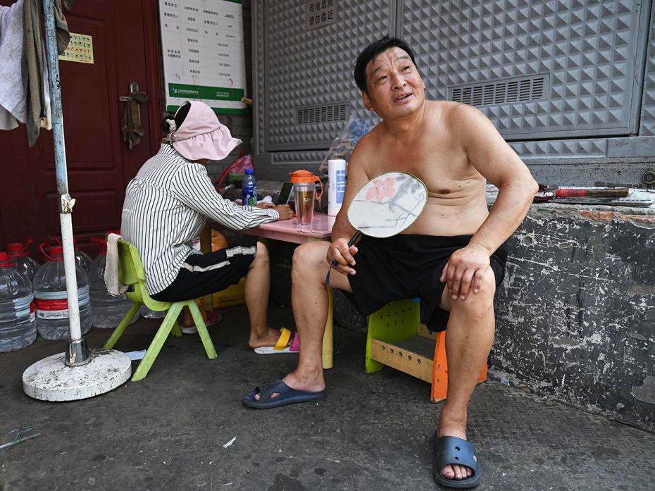 A Chinese man takes a break from fanning himself in an alley during heatwave conditions in Beijing, 